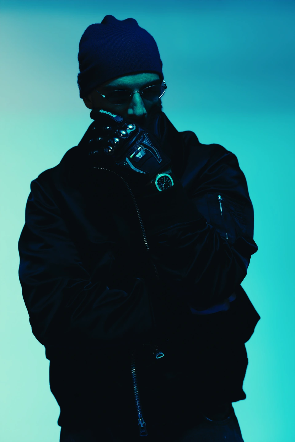 2one2 in a blue beanie and sunglasses, with a gloved hand raised against a cyan backdrop.