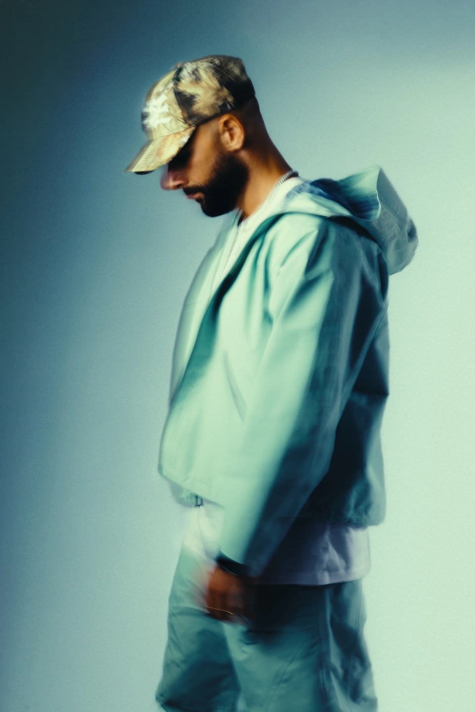 2one2 in a camouflage cap and teal hoodie, photographed in profile.