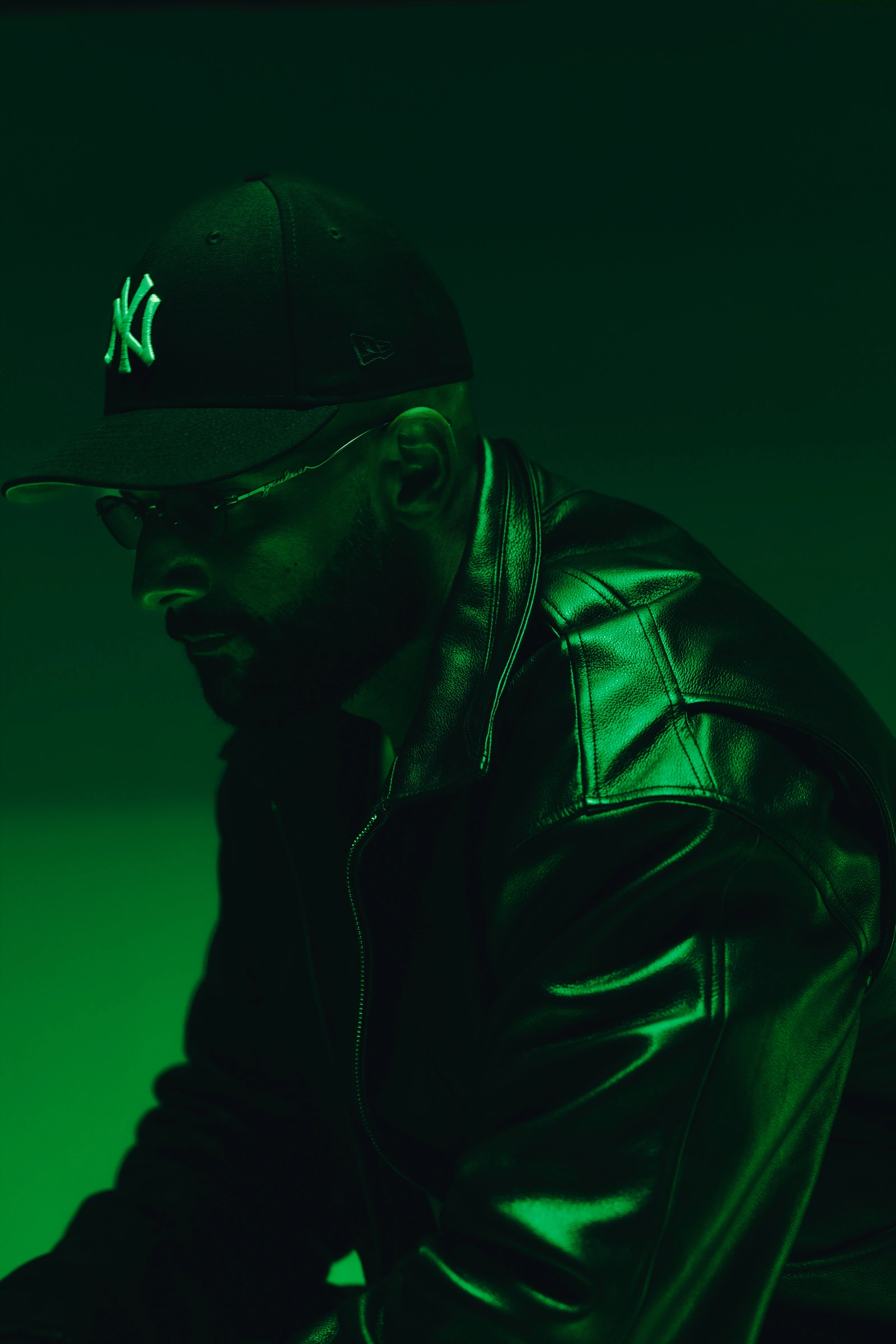 Portrait of 2one2 in a Yankees cap and leather jacket, lit in green.