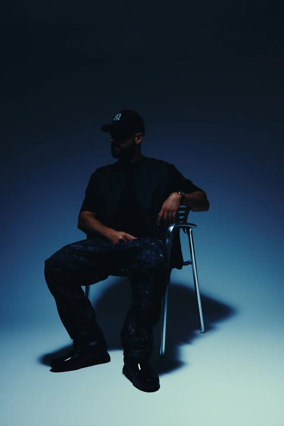 2one2 seated on a chrome chair against a blue studio backdrop.